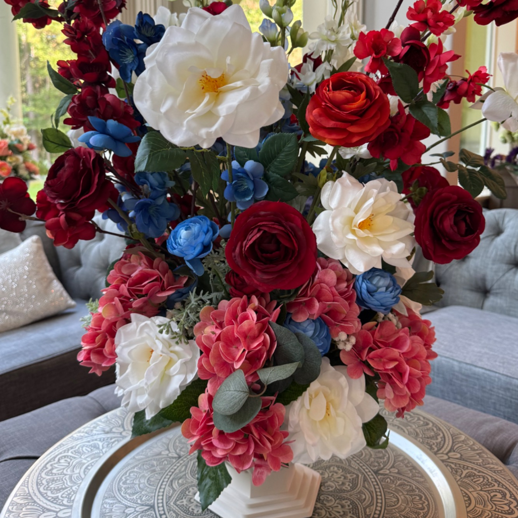 Summer Soirée permanent floral arrangement featuring ivory roses, crimson blooms, blue florals, blush hydrangeas, and eucalyptus in a white Palais Bowl.