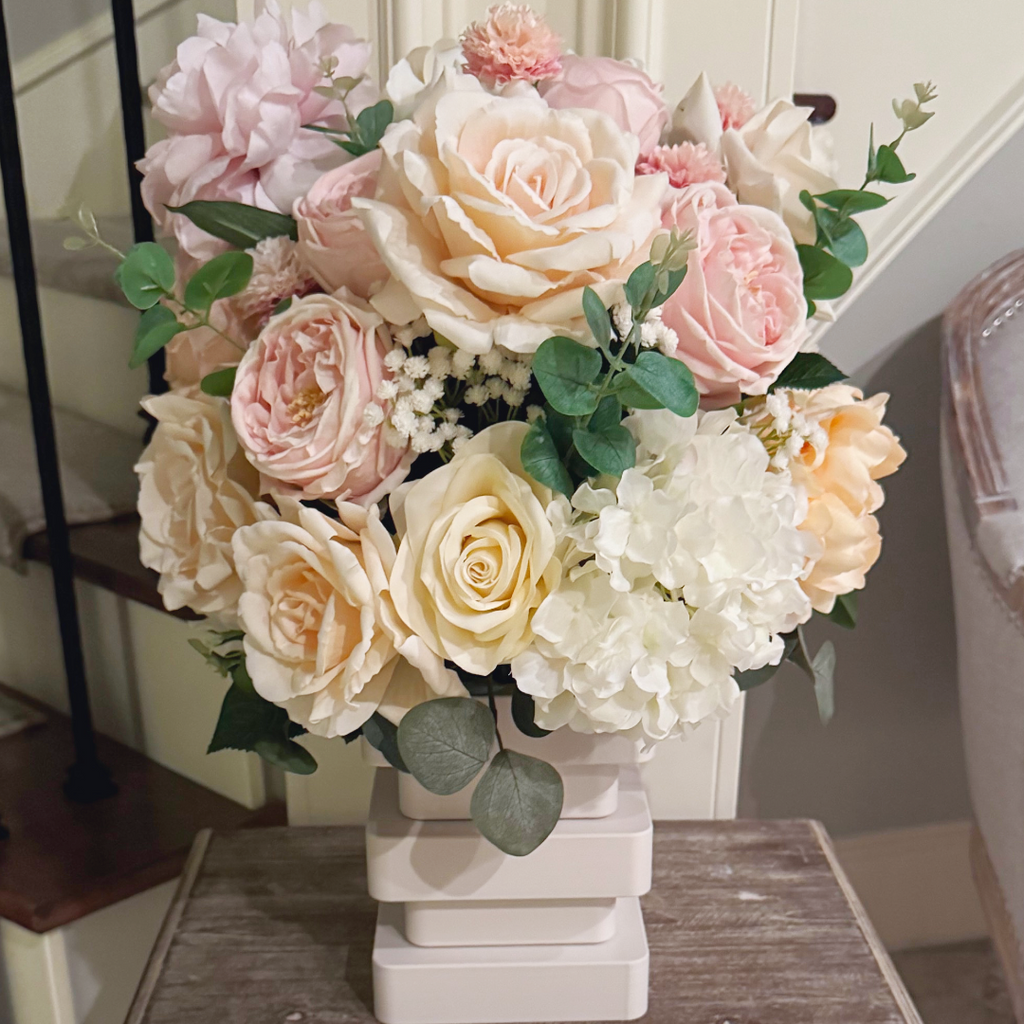 Atelier floral arrangement in the Bone White finish, Duchess size, Rosé Champagne palette displayed on a side table, featuring lifelike blush peonies, garden roses, hydrangeas, and eucalyptus.