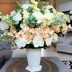 Grand Palais Premium Collection permanent floral arrangement in the Peaches & Cream palette featuring layered ivory peonies, cream roses, peach cymbidium orchids, creamy delphiniums, and eucalyptus in a white Grand Palais Bowl.