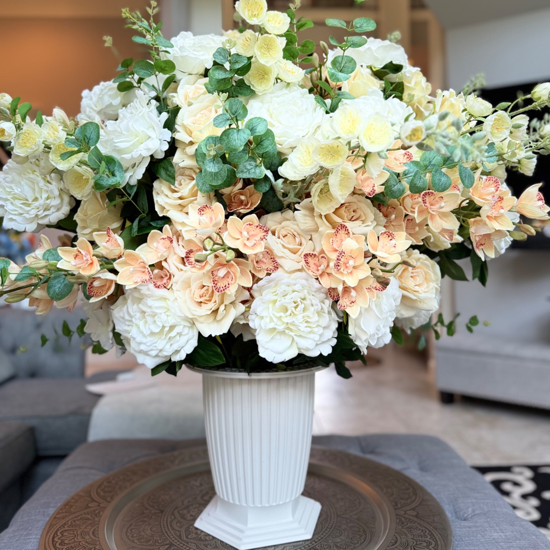 Grand Palais Premium Collection permanent floral arrangement in the Peaches & Cream palette featuring layered ivory peonies, cream roses, peach cymbidium orchids, creamy delphiniums, and eucalyptus in a white Grand Palais Bowl.