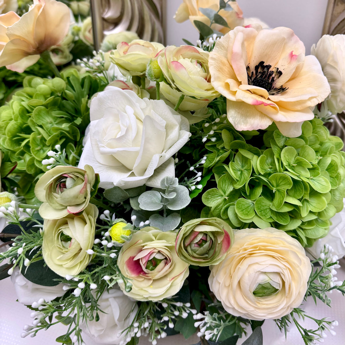 Close-up of green hydrangeas, ivory roses, cream ranunculus and soft greenery in the Signature Duchess floral arrangement.