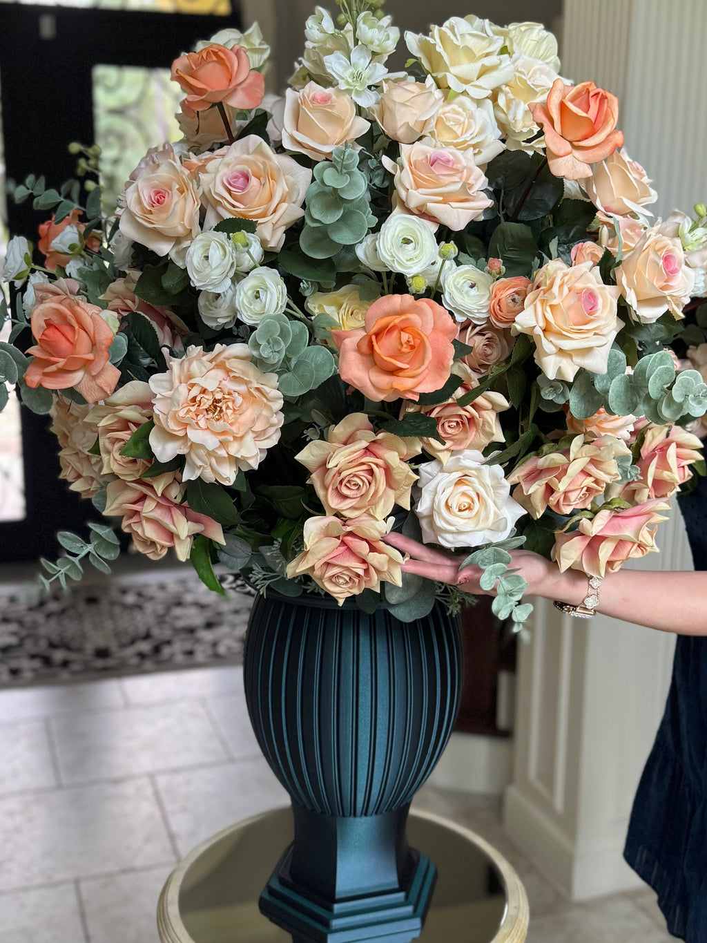 Grand-scale D&W Remembrance Column Vase memorial arrangement in Peaches & Cream with peach, cream and blush permanent florals shown for scale