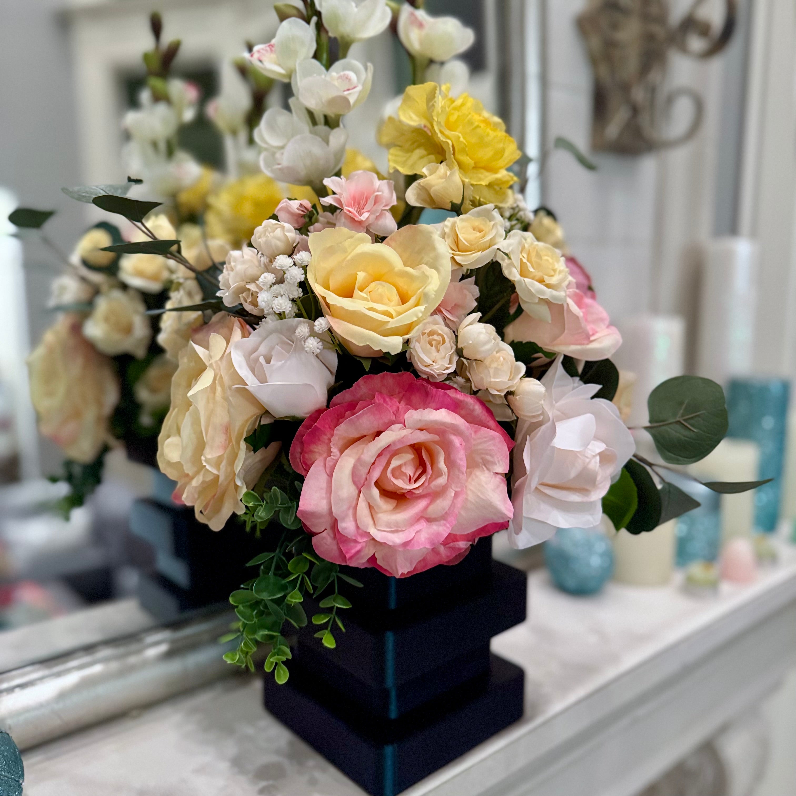 Floral arrangement with pink, yellow, and white flowers on a dark square base.
