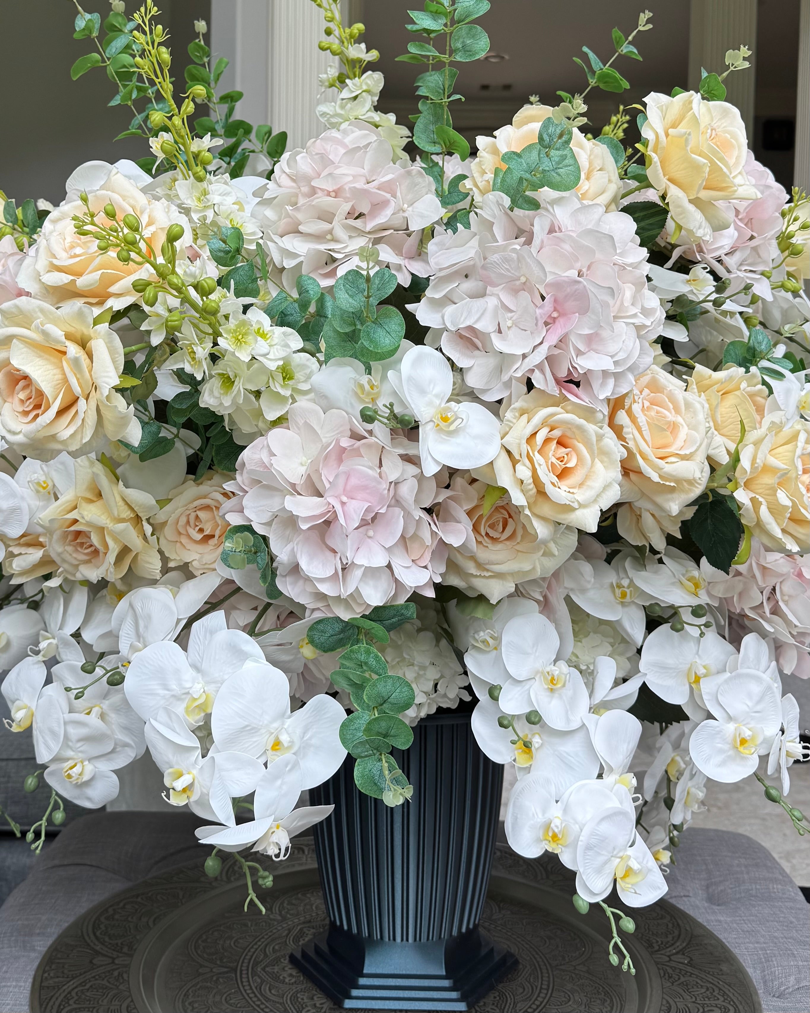 Grand Palais Platinum permanent floral arrangement featuring blush hydrangeas, ivory roses, cascading white orchids, eucalyptus greenery, and premium blooms in a black Grand Palais vessel