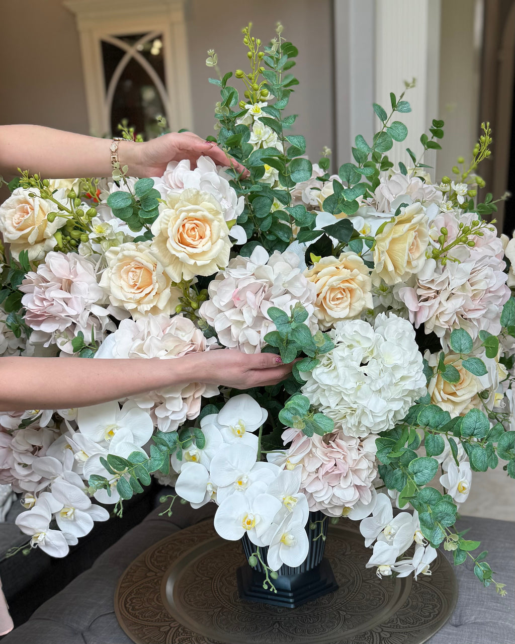Grand Palais Platinum permanent floral arrangement being hand styled with blush hydrangeas, ivory roses, cascading white orchids, eucalyptus greenery, and premium blooms in a black Grand Palais vessel