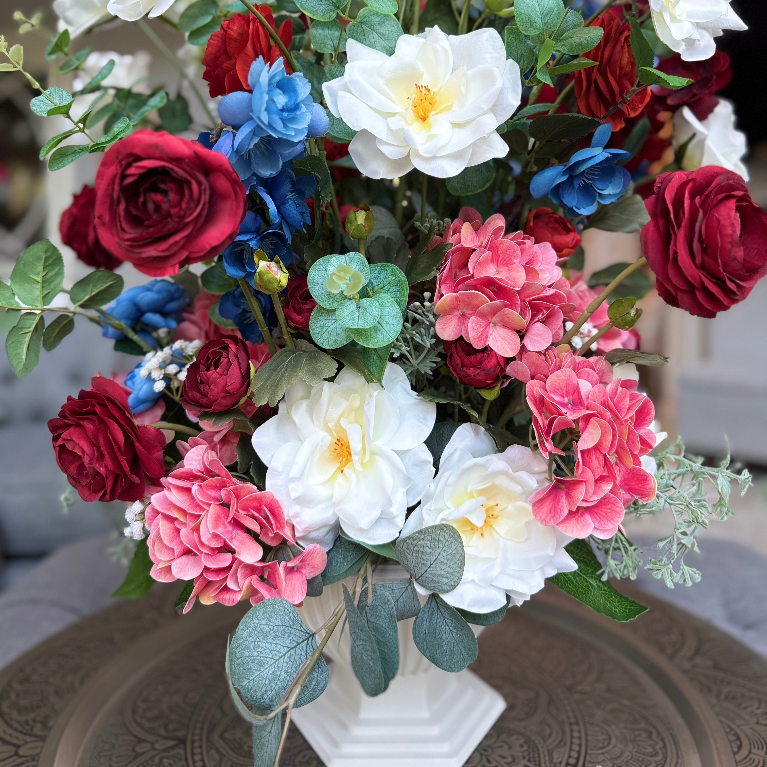 Palais Bowl floral arrangement in the Bone White finish, Queen size, Summer Soirée palette, featuring lifelike white garden roses, deep red ranunculus, blue delphiniums, pink hydrangeas, and eucalyptus.