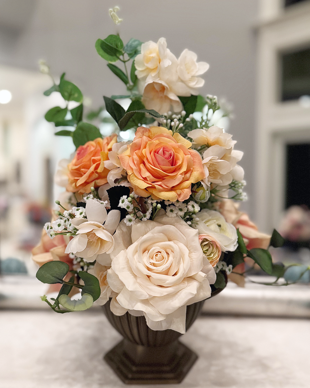 Palais Bowl floral arrangement in the Warm Bronze finish, Duchess size, Peaches & Cream palette, featuring lifelike peach and cream roses, ranunculus, blossoms, baby's breath, and eucalyptus.