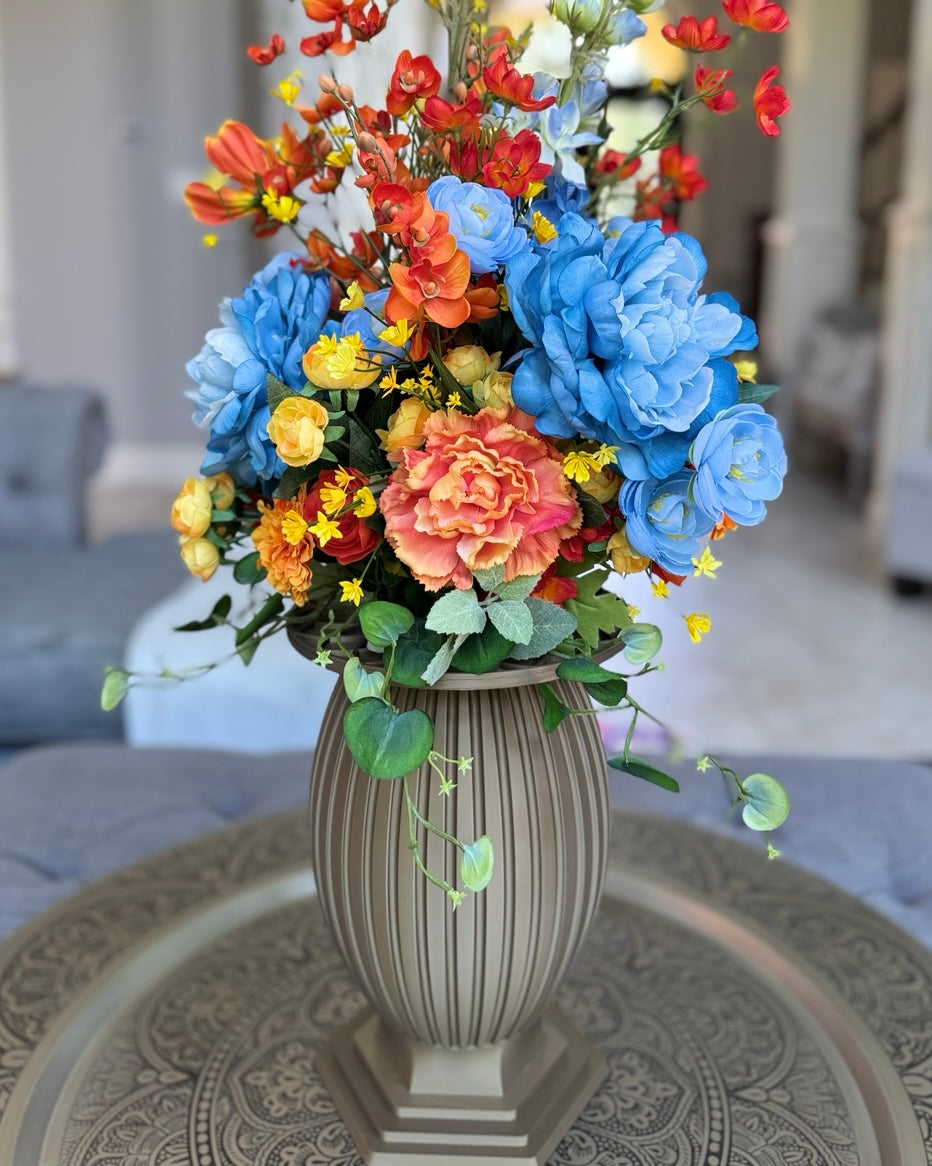 Column Vase floral arrangement in the Warm Bronze finish, Queen size, Sunset Meadow palette, featuring lifelike blue peonies, coral roses, orange orchids, yellow ranunculus, and eucalyptus.