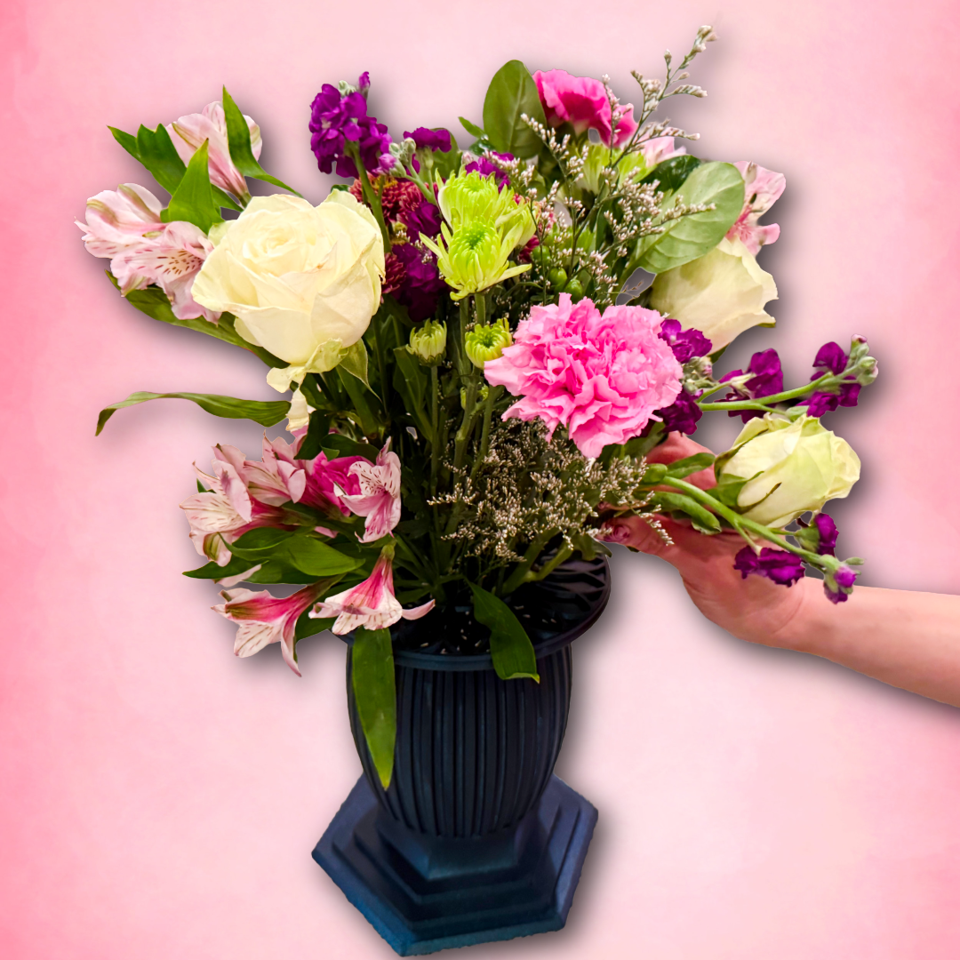 Bouquet of flowers in a dark blue vase held by a hand against a pink background