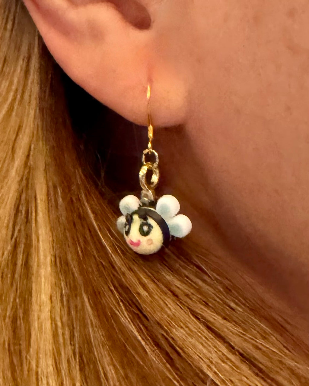 Bee Happy dangle earring with sterling silver hook worn on ear, featuring an artist-designed bee charm with white wings and hand-painted details.