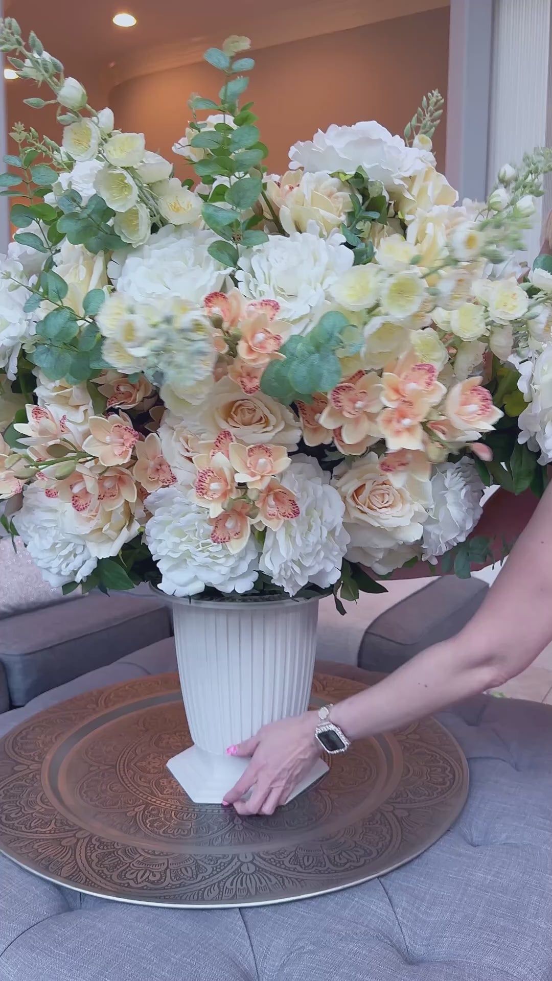Video showing the Grand Palais Premium permanent floral arrangement in the Peaches & Cream palette being carried from a coffee table and styled on a staircase, featuring lifelike ivory, cream, and soft peach blooms with eucalyptus in the Bone White Grand Palais Bowl.